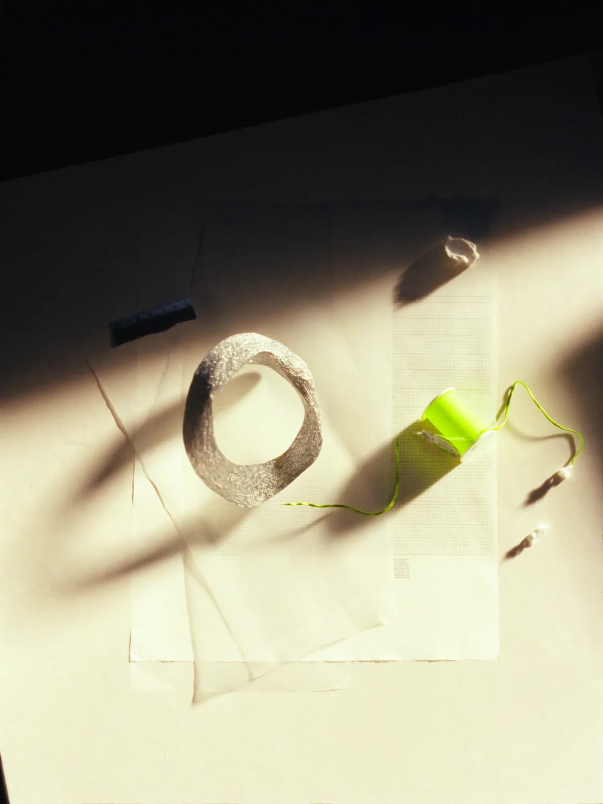 A material study in paper, aluminium and green thread in directional sunlight.
